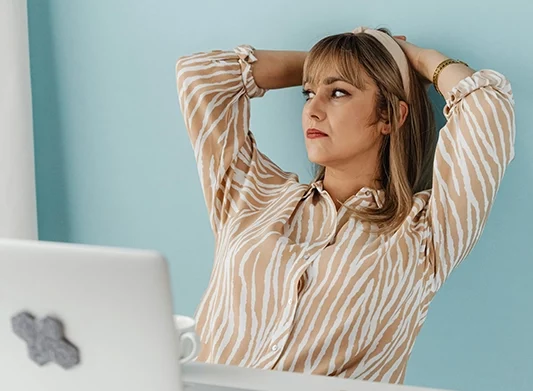 Photo d'une femme en télétravail adossée à sa chaise, qui se pose des questions